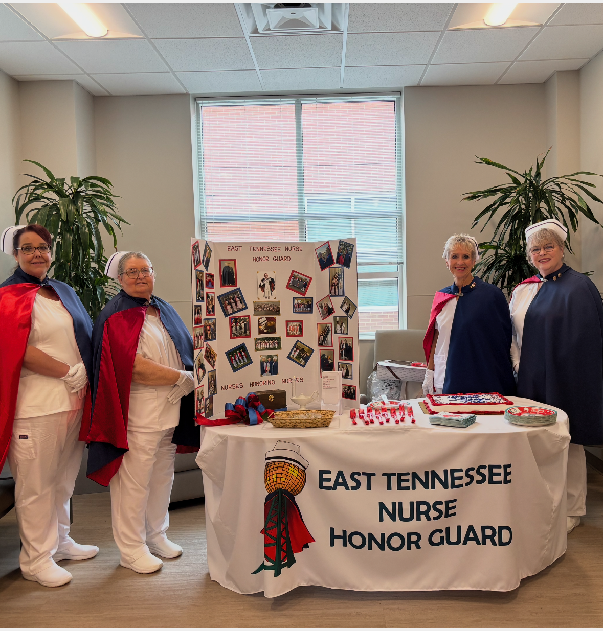 Four honor guard members in uniform standing beside a red-draped information table in a hospital lobby in 2024.