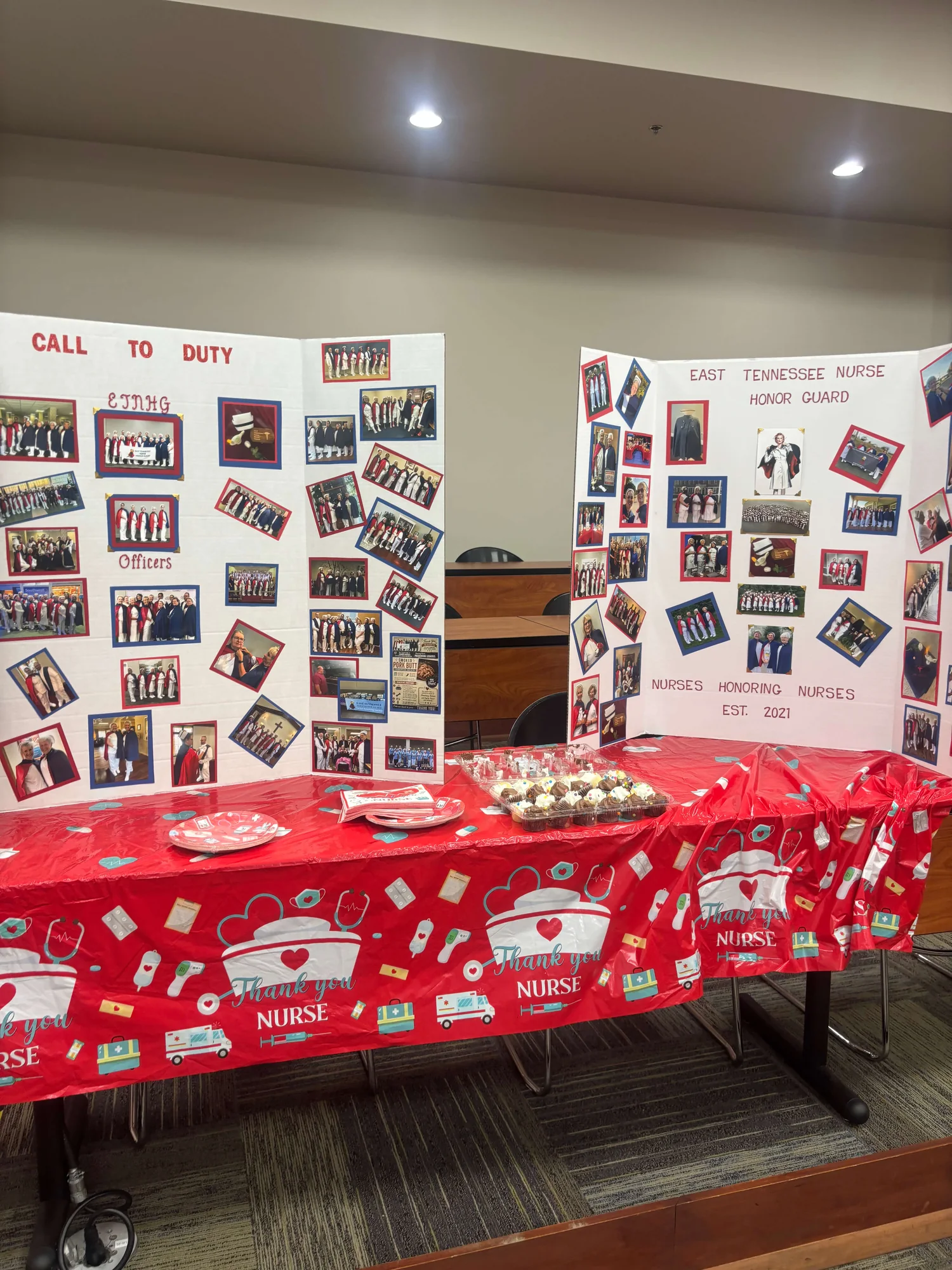 Two trifold display boards covered with photographs from the chapter’s services — one headed “Call to Duty”, the other “East Tennessee Nurse Honor Guard — Nurses Honoring Nurses, Est. 2021” — behind a table laid with a “Thank You Nurse” cloth, matching plates and a tray of cupcakes.
