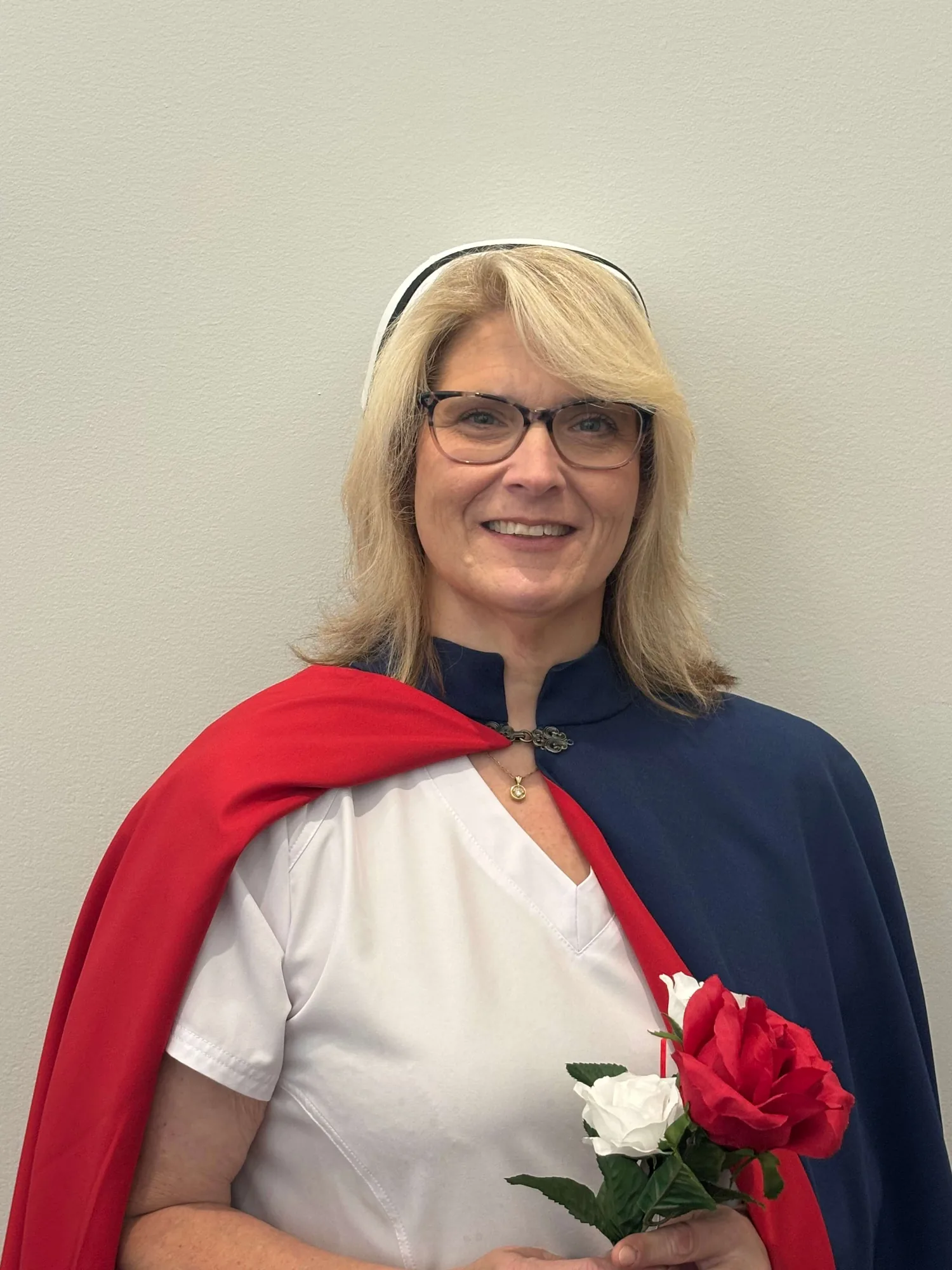 Gloria McMahan, RN, a charter member of the East Tennessee Nurse Honor Guard, in a white uniform, banded cap and red and navy cape, holding a red and a white rose.