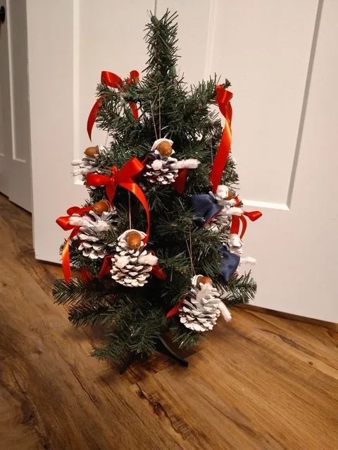 A small Christmas tree trimmed with red ribbon and pinecone ornaments dressed as nurses in white caps.