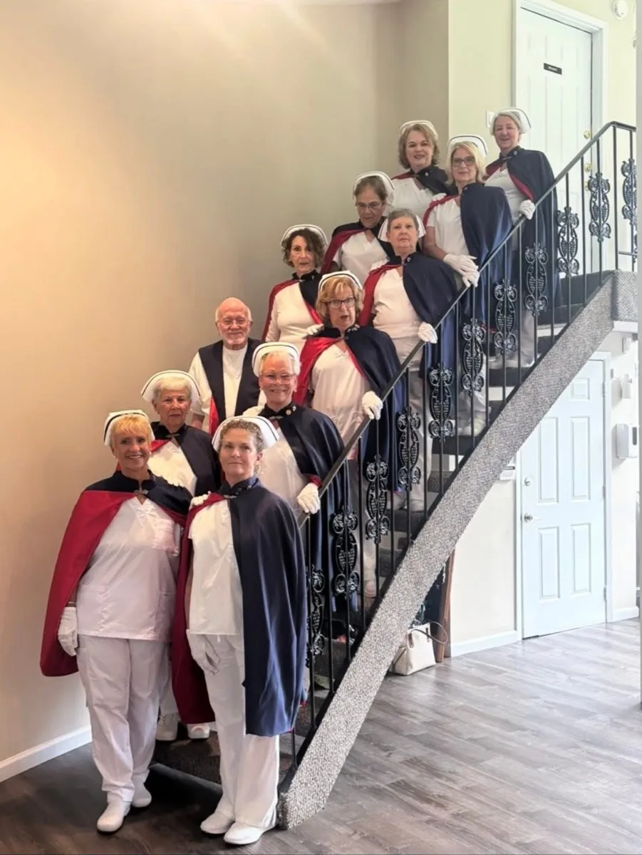 The chapter's earliest group photograph, members in white uniforms and capes gathered on a staircase.