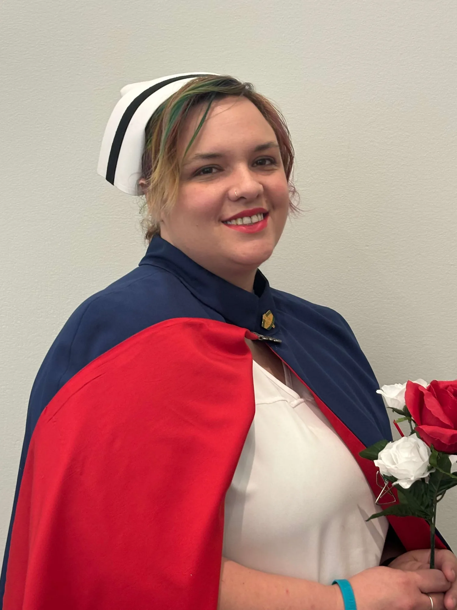 Mollie Elizabeth Kennedy, LPN, founder of the East Tennessee Nurse Honor Guard, in a white uniform, banded cap and red and navy cape, holding a red and a white rose.