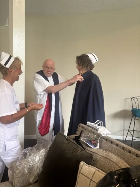 Three honor guard members getting ready for a service, one helping another fasten a cape while a third looks on.