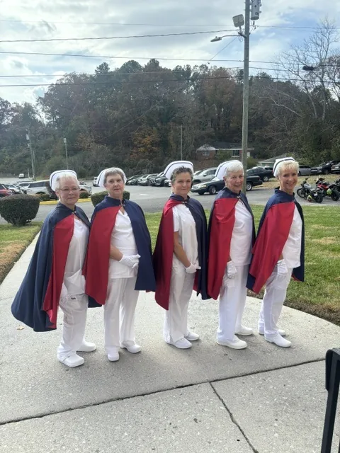 Five honor guard members standing in line on a walkway outside a funeral home on an autumn afternoon.