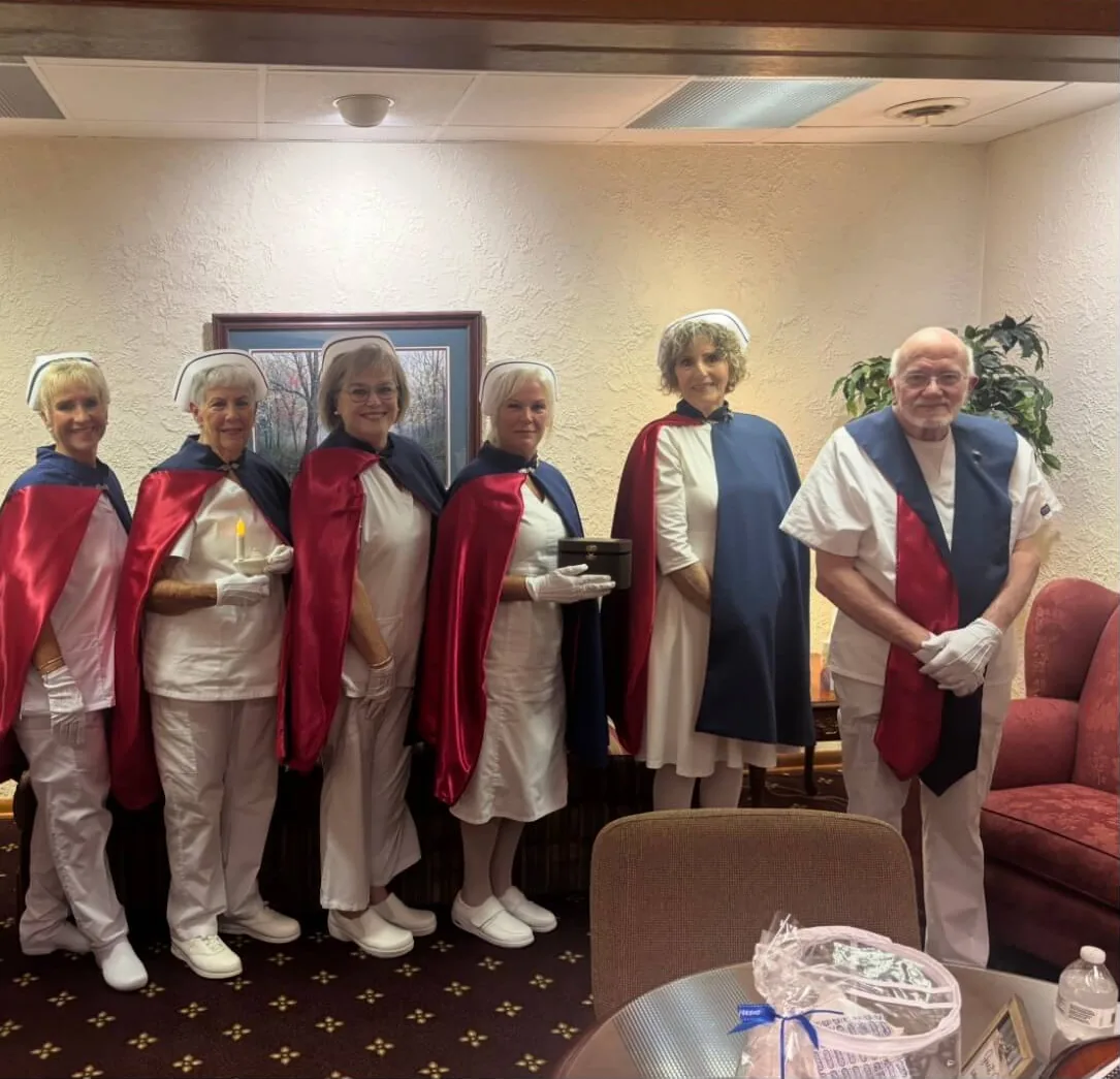 Honor guard members in white uniforms and capes standing together in a family sitting room before a tribute.