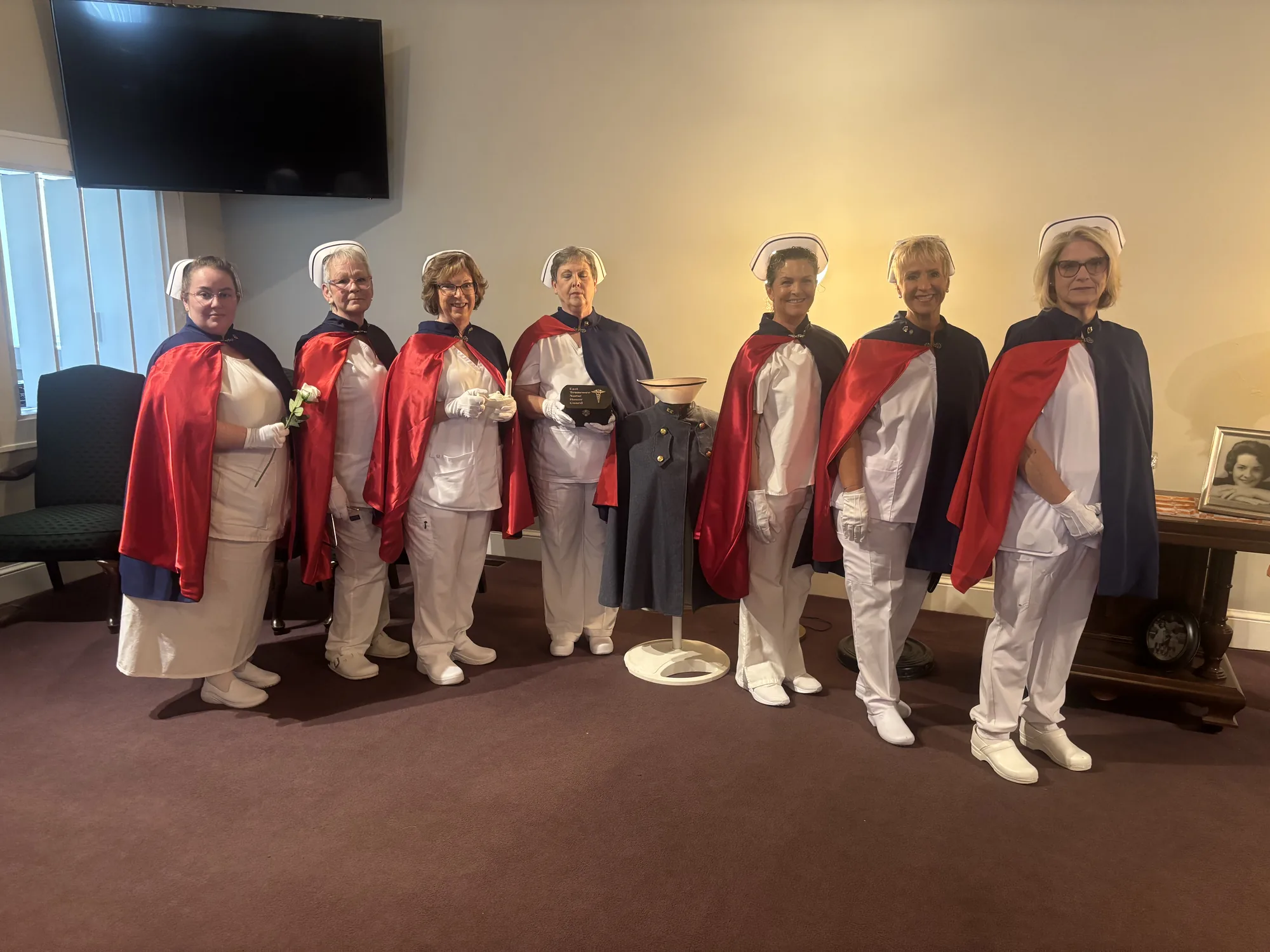 Seven honor guard members standing in formation with white roses and a Nightingale lamp in a funeral home chapel.