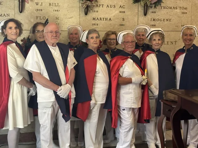 The honor guard standing together in front of a mausoleum wall of engraved memorial niches decorated with small flags and wreaths.