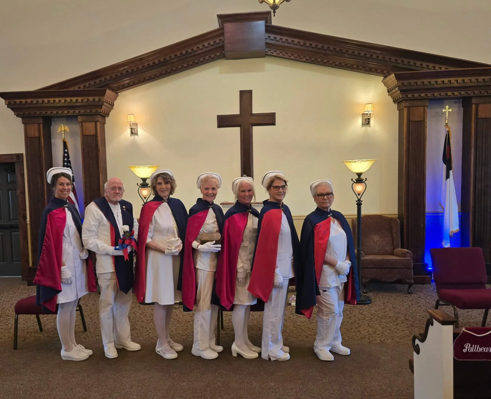 Eight honor guard members standing in formation before a wooden cross at the front of a chapel.