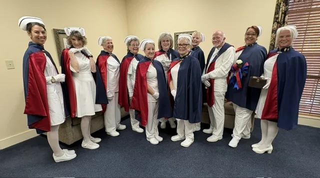 Eleven honor guard members standing shoulder to shoulder in a funeral home family room, one carrying the Nightingale lamp.
