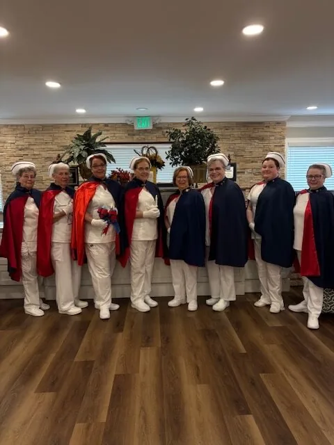 Honor guard members in white uniforms and capes standing in a line across a wooden floor before a service begins.