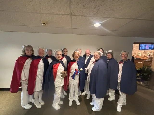 Twelve honor guard members standing together at the front of a chapel, one holding the Nightingale lamp and another a white rose.