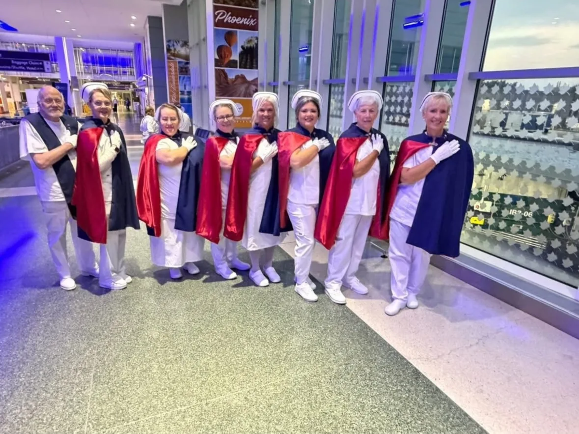 Eight honor guard members standing in a row with hands over their hearts beside the terminal windows at night.