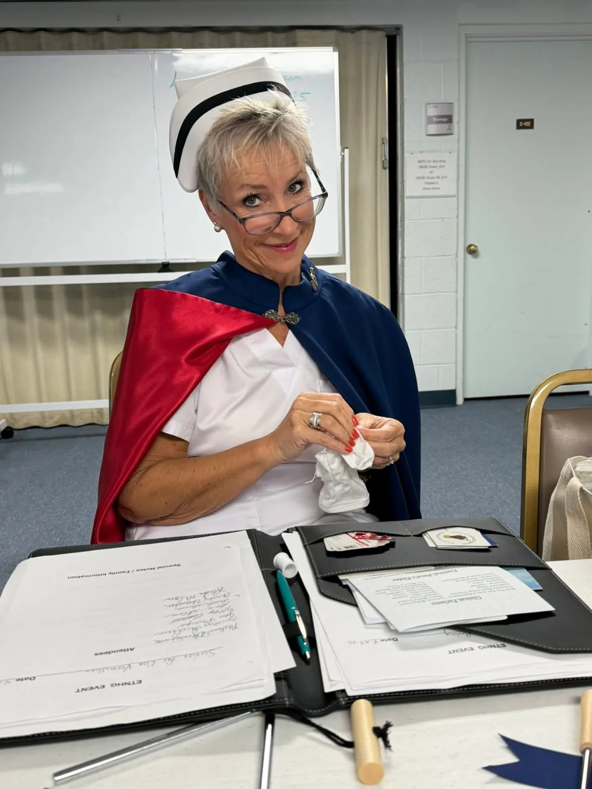 The same member looking up from the table with the mended white glove in hand, needle and thread put away, ready for the ceremony.
