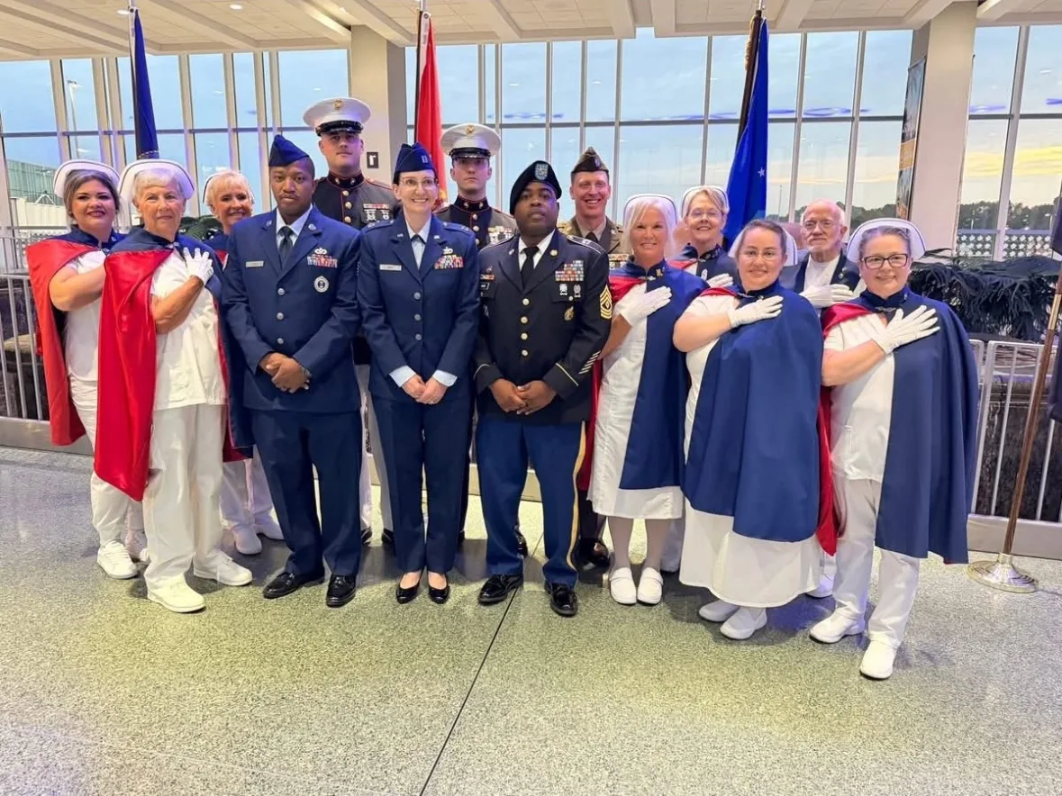 Honor guard members and Air Force personnel posed together in an airport terminal.