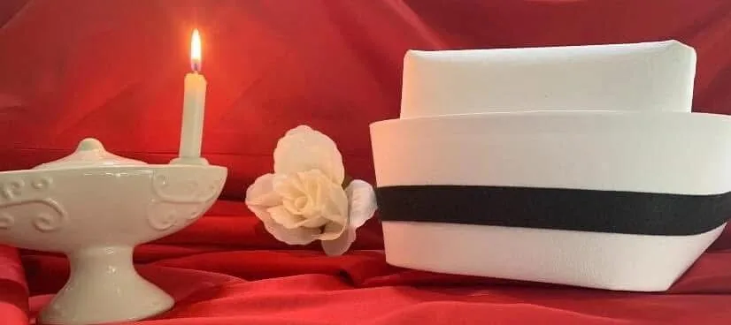 A lit Nightingale lamp, a pale rose and a banded white nurse's cap arranged on red fabric.