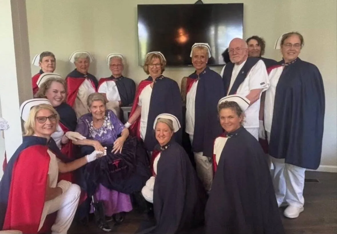 Honor guard members in uniform gathered around Marge Bryant, RN, seated in the centre, during her Living Tribute on 8 August 2025.