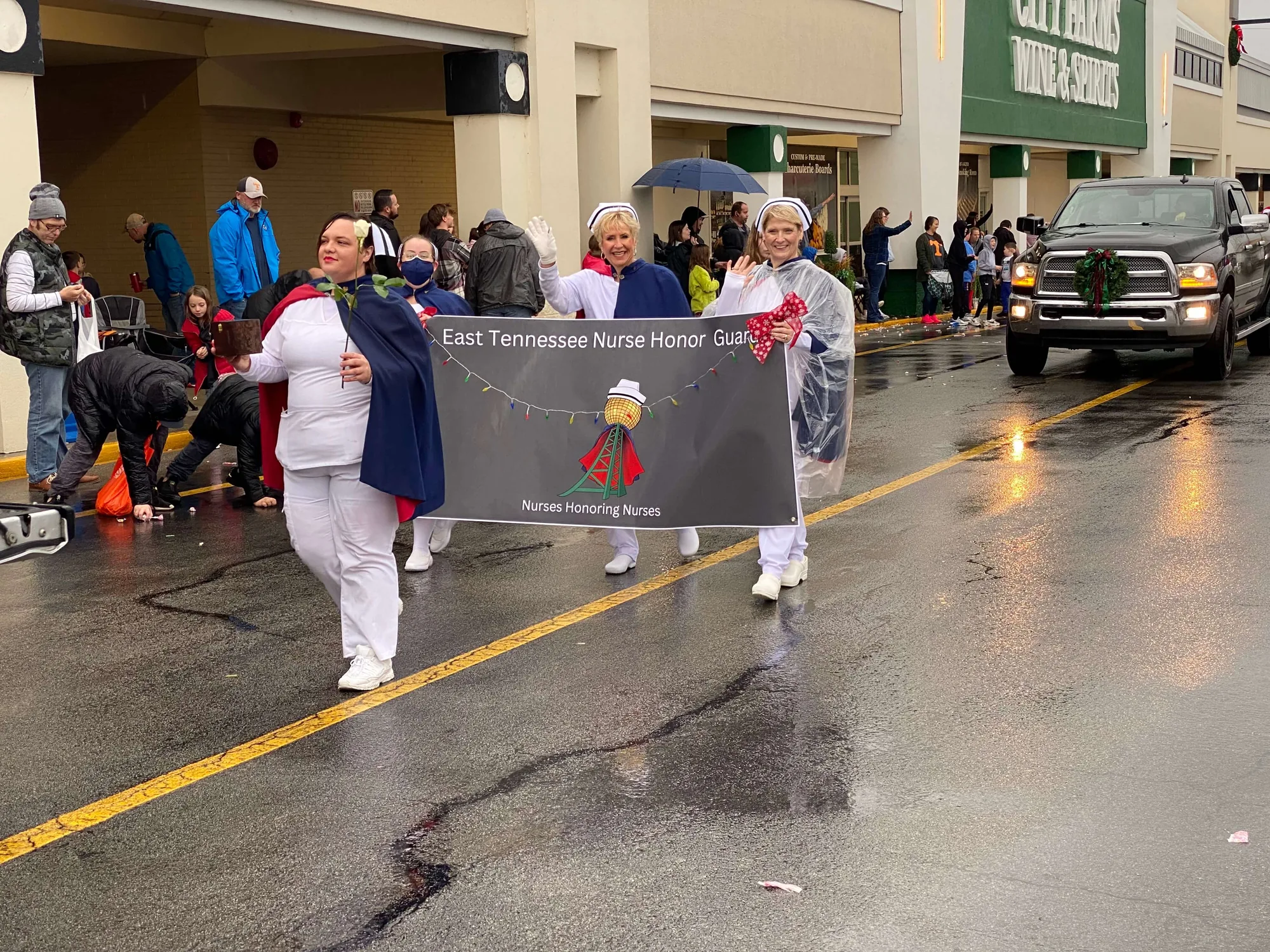 Honor guard members in capes carrying the East Tennessee Nurse Honor Guard banner down a wet street during the Maryville parade.