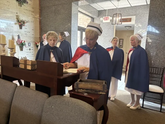 An honor guard member reading from a wooden lectern in a mausoleum while other members stand alongside the memorial niches.