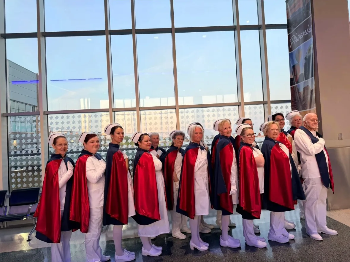 A line of honor guard members in capes standing along the tall windows of an airport terminal.