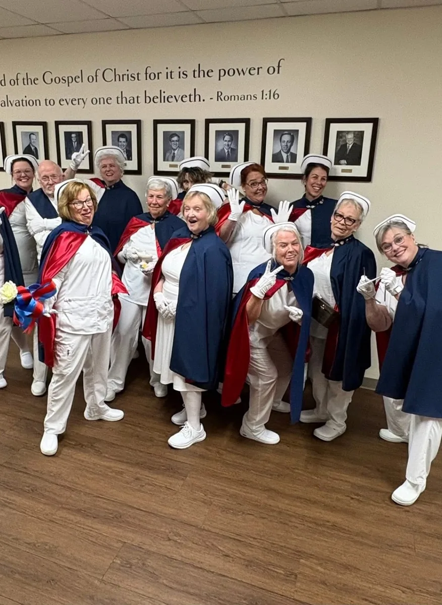 Honor guard members in capes waving and laughing together indoors.