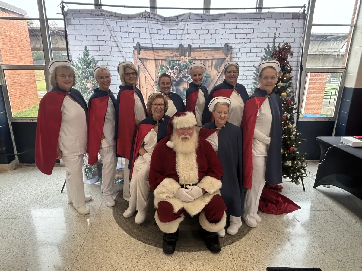 Honor guard members in capes gathered around Santa Claus in front of a Christmas tree.