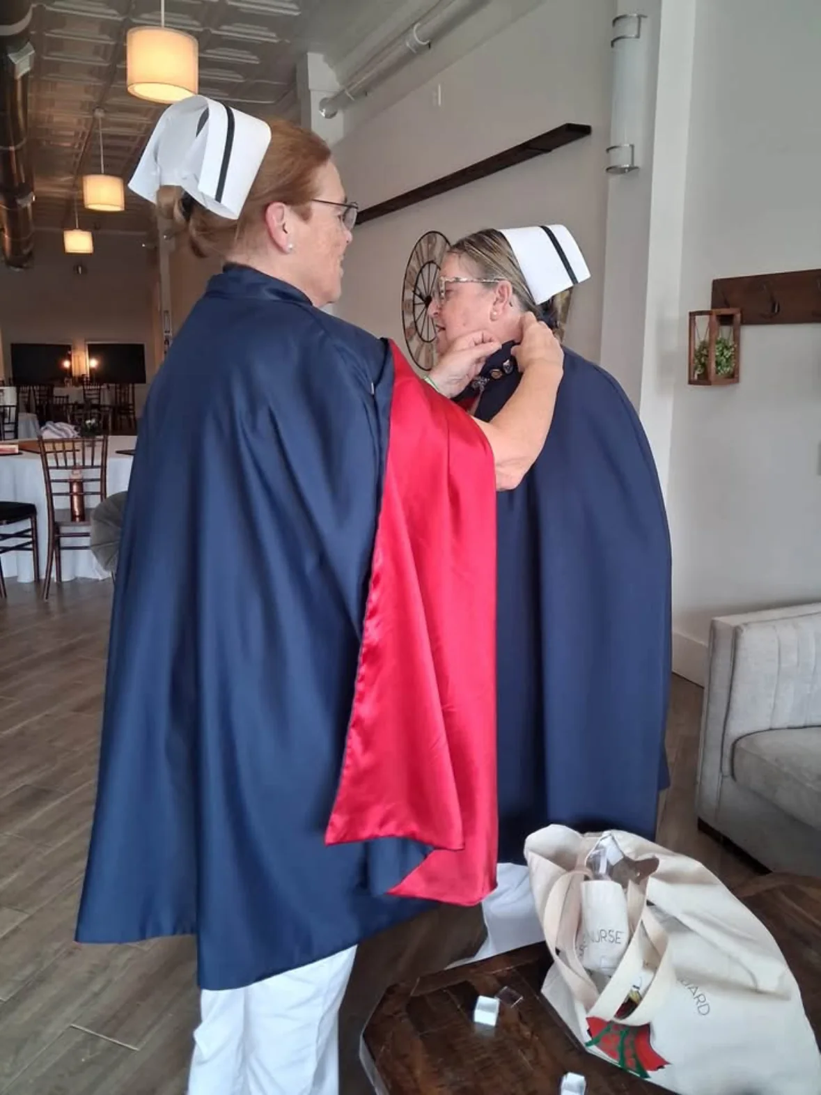 Mary Cantrell being pinned for 25 services by Barbara Moore, both in navy capes and banded nurse's caps.