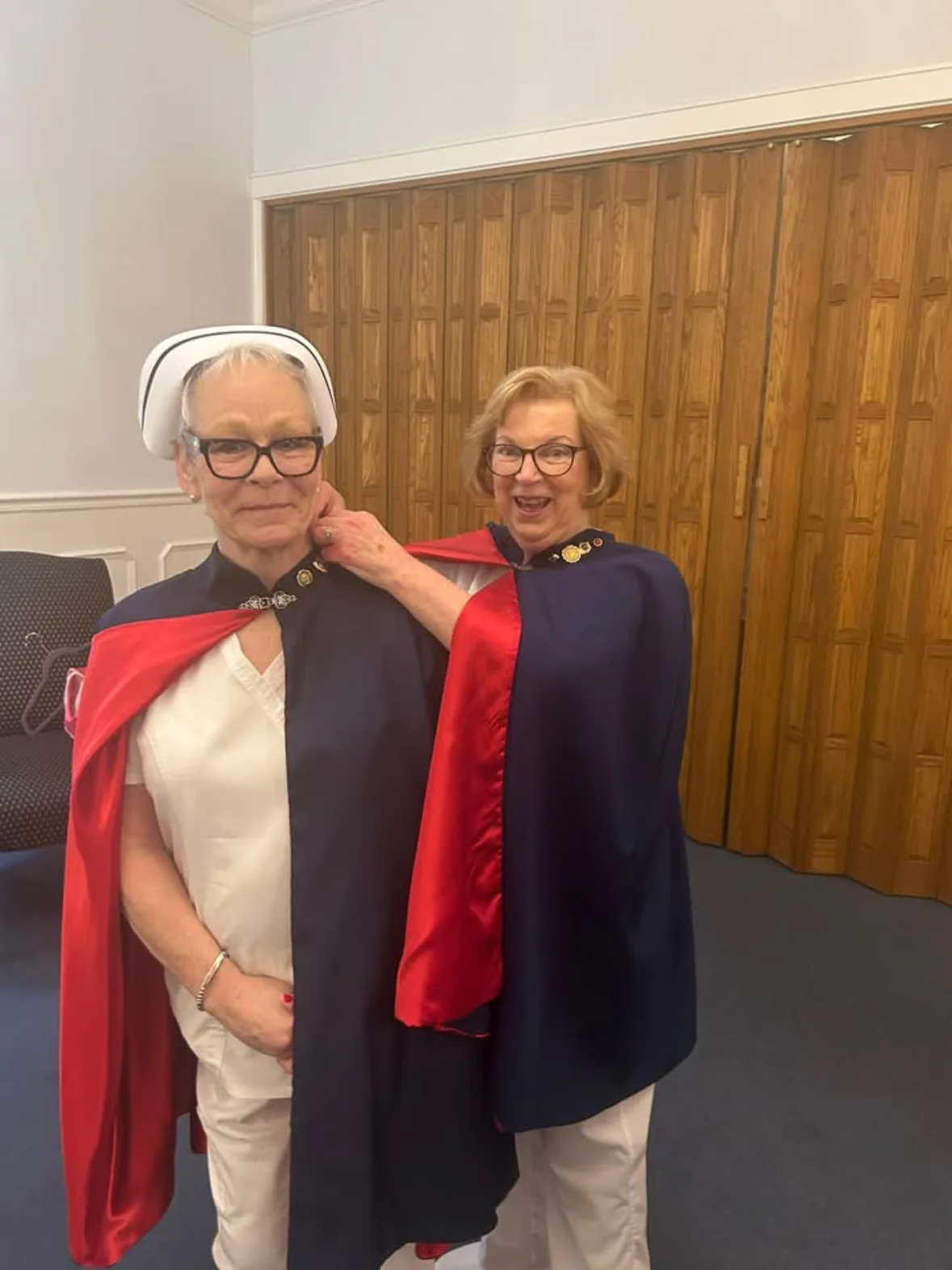 Bridgette Caldwell in a white uniform, cape and banded nurse's cap standing beside Jan Phillips, who has just pinned her for 50 services.