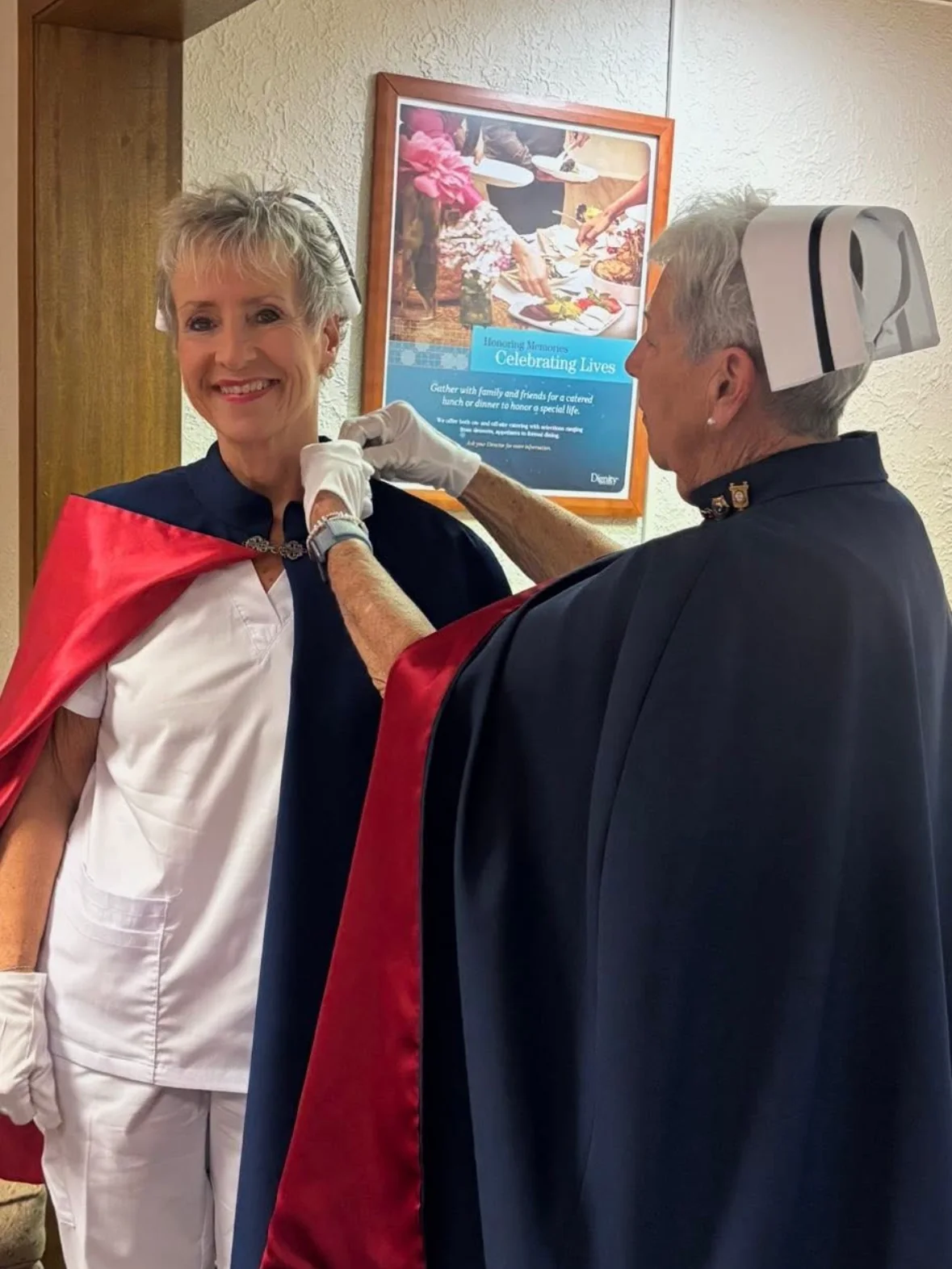 Melanie Pfennigwerth in a white uniform and red-lined cape being pinned for 50 services by Ann Allen.