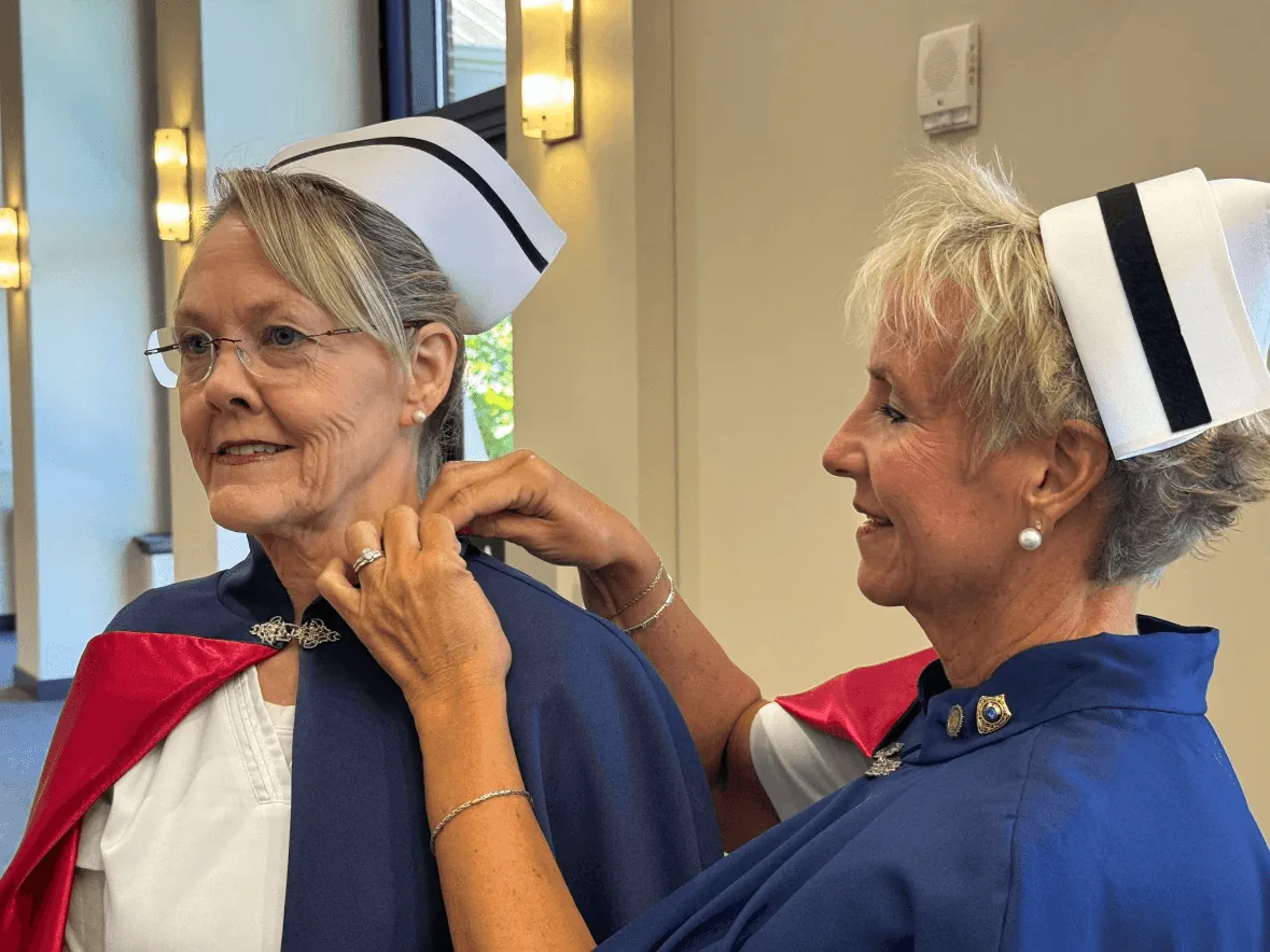 Diana Thompson-Wojnowski, in white uniform and cape, being pinned by Melanie Pfennigwerth to mark a first service with the East Tennessee Nurse Honor Guard.
