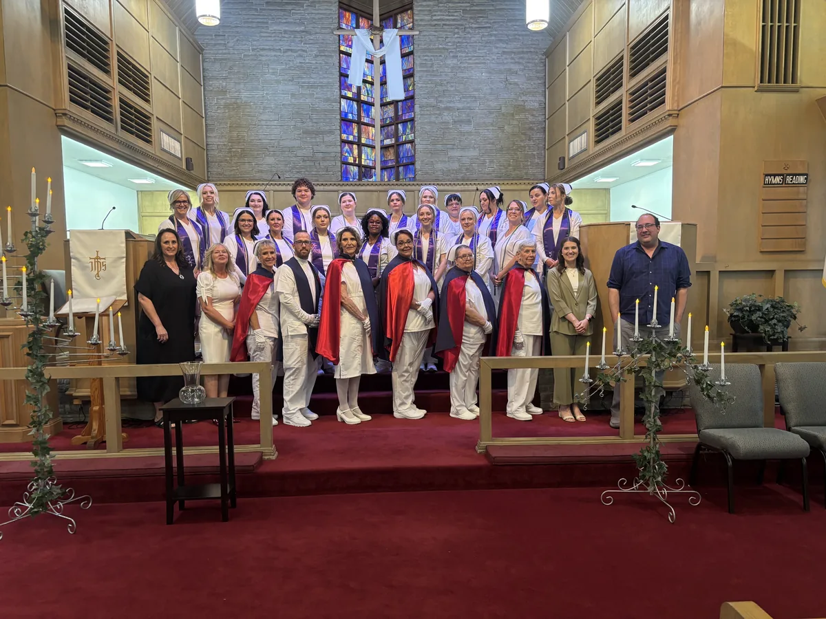 Honor guard members standing with nursing graduates and faculty at a graduation ceremony in a chapel.