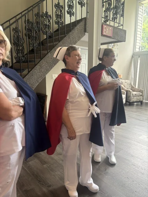Two honor guard members in capes standing beside a staircase in a funeral home before a tribute, one of them holding a white rose.