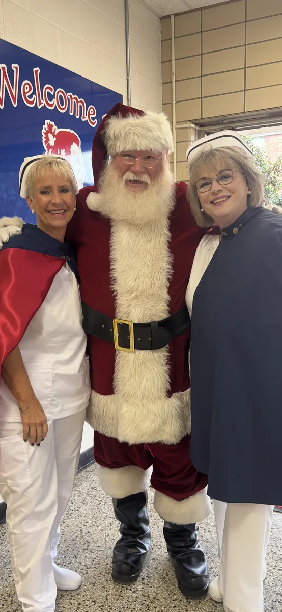 Two honor guard members in uniform standing on either side of Santa Claus beside a welcome sign.