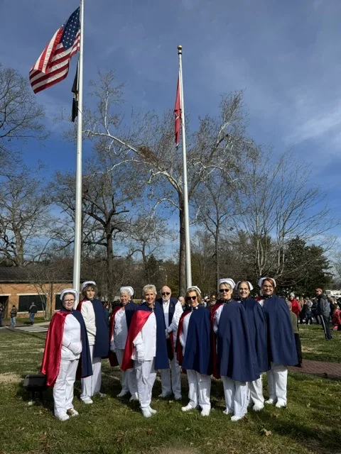The honor guard standing together beneath the United States, POW-MIA and Tennessee flags at a Wreaths Across America ceremony, with a crowd gathered behind them.